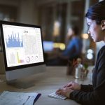 Young businesswoman examining business charts on desktop PC in the office.