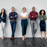 5 young professionals standing in a line against a wall, arms folded and smiling