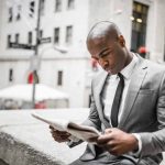 African American male reading a newspaper on a city street