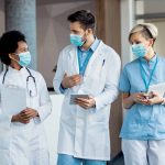 Group of medical experts with face masks talking while walking through a hallway