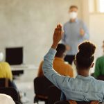 Student raising hand among students in classroom