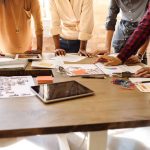 Photo of wooden table in an office with people standing around it with their hands on the table